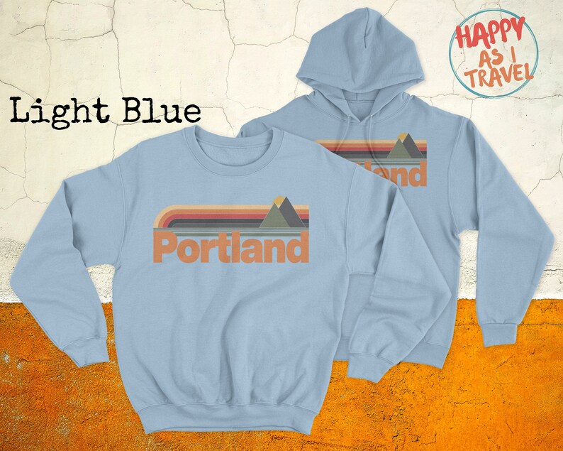 May include: Light blue sweatshirt with a retro-style graphic of mountains and the word "Portland" in a vintage font.