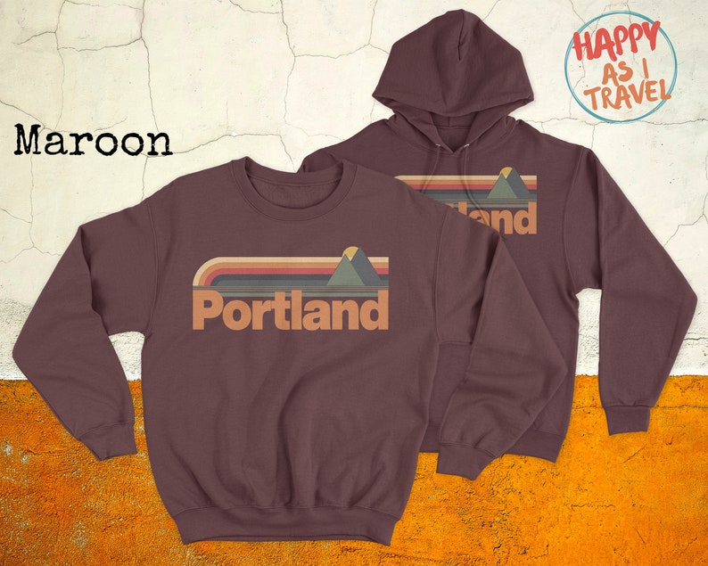 May include: Two maroon sweatshirts featuring a retro-style graphic of a mountain range and the word "Portland". The hoodie has a drawstring and the crewneck has a relaxed fit.