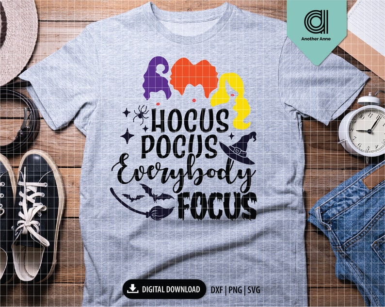 May include: A heather gray t-shirt with the text "Hocus Pocus Everybody Focus" in black script. The design includes silhouettes of witch hair in purple, orange, and yellow, a witch hat, a spider, and a bat. The shirt is a digital download.