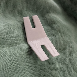 May include: A white, 3D-printed plastic tool. It has a flat, rectangular base with two parallel, U-shaped cutouts. The tool is angled and likely designed for a specific purpose. The measurements are in centimeters.