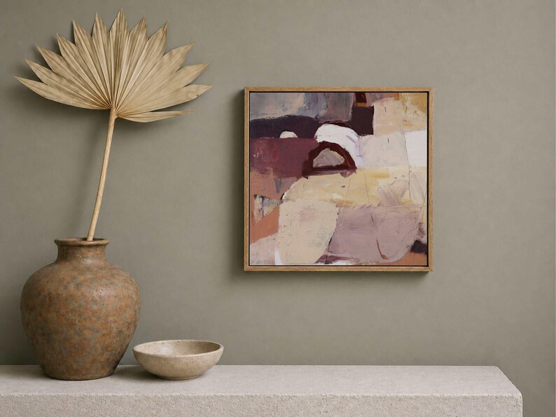 Pu&ograve; includere: Dipinto di arte astratta in una cornice di legno con una tavolozza di colori neutri beige, marrone e bordeaux. Una foglia di palma secca in un vaso marrone e una piccola ciotola su una superficie bianca.