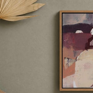 Pu&ograve; includere: Stampa artistica astratta in una cornice di legno naturale. L'opera presenta una miscela di toni bordeaux, crema e beige. Una foglia di palma secca e un vaso di terracotta sono in primo piano.