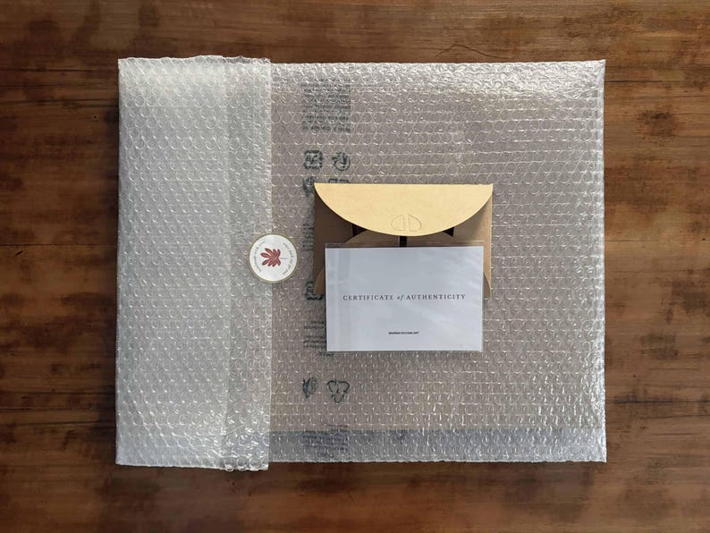 Pu&ograve; includere: Una vista dall'alto mostra un pacco avvolto in pluriball. All'interno, una busta di carta kraft e una carta con la scritta "CERTIFICATE OF AUTHENTICITY" sono visibili. &Egrave; incluso anche un adesivo rotondo con un disegno a foglia.