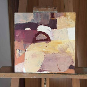 Pu&ograve; includere: Dipinto astratto su tela quadrata, con una tavolozza di colori tenui. L'opera presenta una composizione di forme a strati nei toni del beige, bordeaux e bianco, con pennellate visibili. Il dipinto &egrave; esposto su un cavalletto di legno.