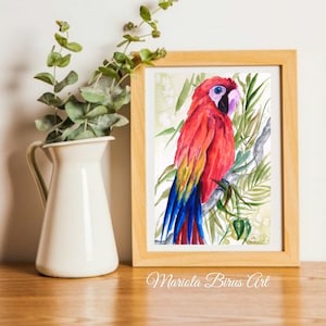 May include: Watercolor painting of a red and yellow macaw perched on a branch with green leaves. The painting is framed in a light wood frame and has the artist's signature in the bottom right corner.