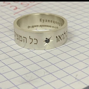 Puede incluir: Un anillo de plata con un diamante negro engastado en forma de estrella. El anillo está grabado con el texto "Кузнецову" y "От души душевно исб..." en escritura cirílica y "כל החיים" en hebreo.