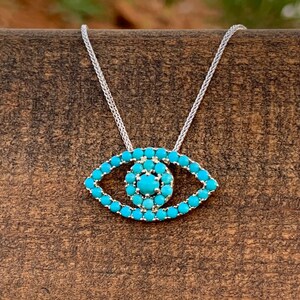 Puede incluir: Un collar de cadena de plata con un colgante de ojo turco turquesa. El colgante est&aacute; hecho de peque&ntilde;as piedras turquesas engastadas en plata.