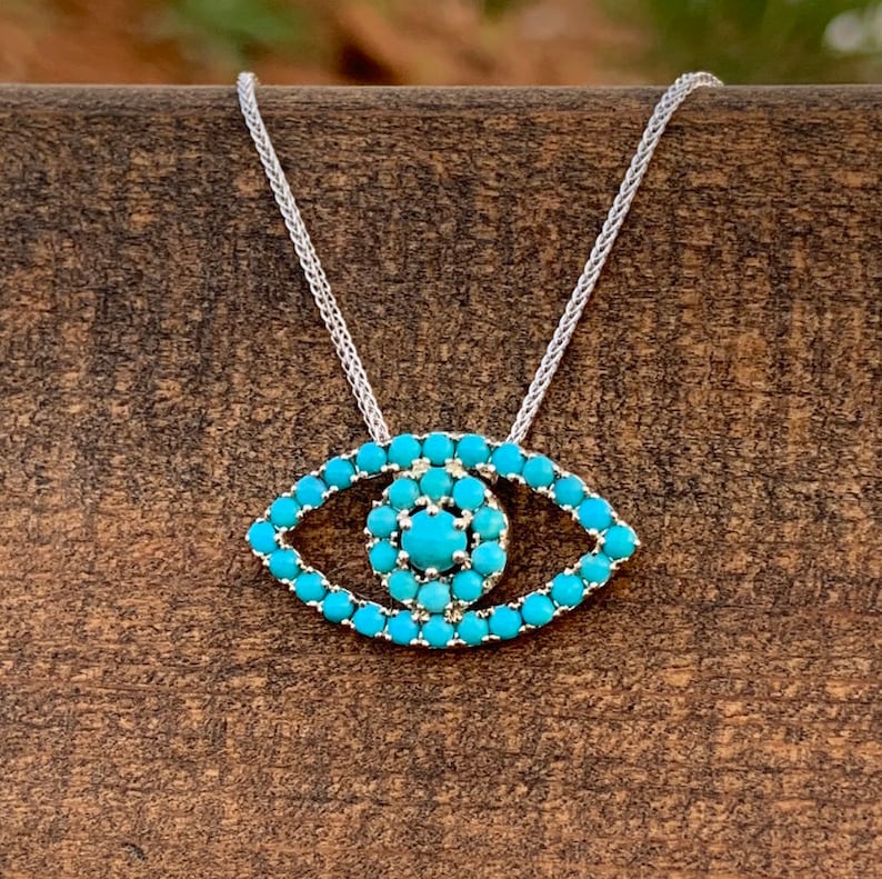 Puede incluir: Un collar de cadena de plata con un colgante de ojo turco turquesa. El colgante est&aacute; hecho de peque&ntilde;as piedras turquesas engastadas en plata.