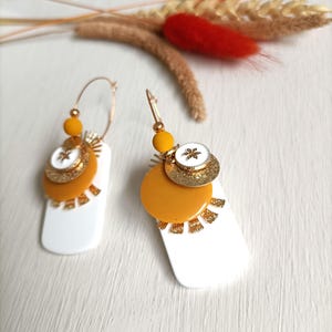 Gouden ovale hangende oorbellen, gelakte witte rechthoekige paillettenaccumulatie, mosterdgele pailletten, wit medaillon, gouden hangers
