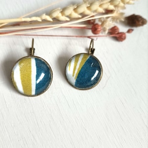 Op de afbeelding: Een paar ronde, bronzen oorbellen met een blauw, wit en geel stoffen ontwerp. De stof is zichtbaar door het heldere glas.