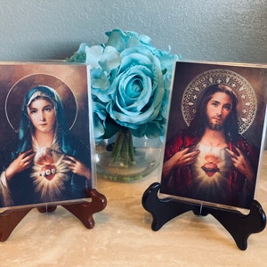 May include: Two framed religious images with a gold background. The image on the left is of the Virgin Mary with a blue robe and a crown of thorns. The image on the right is of Jesus with a red robe and a crown of thorns. Both images have a heart with a crown of thorns.
