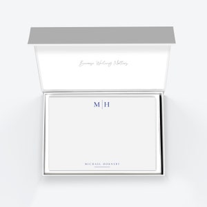 May include: An open white box with a grey lid, revealing a stack of white stationery with blue lettering. The stationery features the initials "M|H" and the name "MICHAEL HORNSBY" printed on it. The inside of the box lid has the text "Because Writing Matters" printed in cursive.