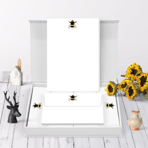 May include: A white box containing a set of stationery featuring a bee design. The box is open, revealing the notepad and envelopes.
