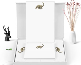 May include: A white box with a set of stationery featuring a dinosaur illustration. The box contains note cards and envelopes.