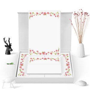 May include: A white box containing a set of pink floral stationery. The box is open, revealing the stationery, which includes letter paper and envelopes with a pink floral border.