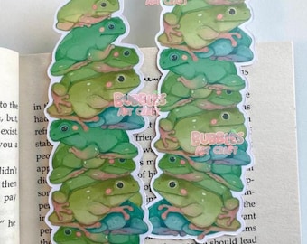 Könnte beinhalten: Zwei Lesezeichen mit Froschmotiven sind auf einem Buch gestapelt. Jedes Lesezeichen zeigt einen Stapel grüner Frösche mit hellgrünen und blauen Akzenten. Der Text "Bubbles Art Craft" ist auf jedem Lesezeichen aufgedruckt.