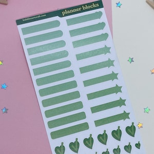 Op de afbeelding: Een vel groene en witte planner stickers met de tekst "planner blocks" in het geel. De stickers bevatten rechthoekige blokken, pijlen en harten.