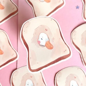 Könnte beinhalten: Ein Set mit Aufklebern, die einen Cartoon-Entenküken zeigen, das aus einem Stück Toast schaut. Die Aufkleber sind auf weißem Papier mit glänzendem Finish gedruckt.