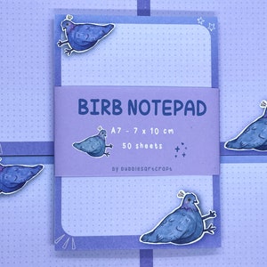 Op de afbeelding: Een paarse notitieblok met een witte rand en een schattige cartoon-duivenillustratie. De notitieblok is gelabeld "Birb Notepad" en heeft de afmetingen A7 - 7 x 10 cm. Het bevat 50 vellen papier.