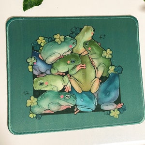 Puede incluir: Una alfombrilla de ratón verde con un diseño de varias ranas verdes sobre un fondo verde con hojas de trébol.