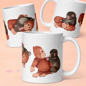 May include: White ceramic mug with a watercolour illustration of orangutans and monkeys. The design shows the animals in various playful poses, in shades of brown and black. The mug has a curved handle.