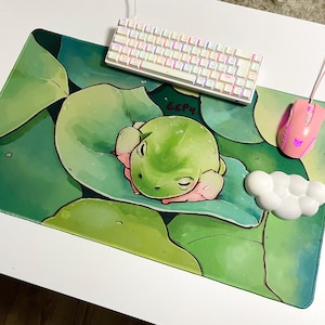 May include: A green frog sleeping on a green and white lily pad with the text "EEPY" written on the lily pad. The frog is surrounded by green lily pads. The background is a white surface.
