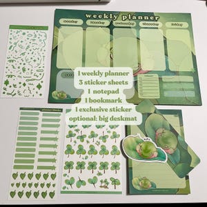 May include: A weekly planner, three sticker sheets, a notepad, a bookmark, and an exclusive sticker featuring a frog design. The planner has a green and white color scheme with a frog illustration. The sticker sheets feature green clover designs. The notepad has a green and white striped design with a frog illustration. The bookmark has a green and white striped design with a frog illustration. The exclusive sticker features a frog illustration.