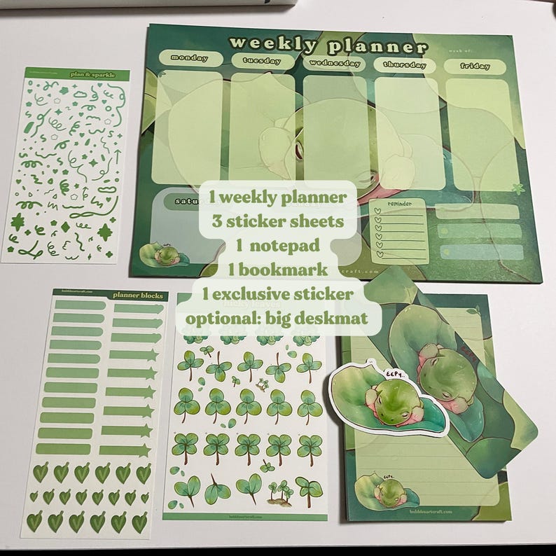 May include: A weekly planner, three sticker sheets, a notepad, a bookmark, and an exclusive sticker featuring a frog design. The planner has a green and white color scheme with a frog illustration. The sticker sheets feature green clover designs. The notepad has a green and white striped design with a frog illustration. The bookmark has a green and white striped design with a frog illustration. The exclusive sticker features a frog illustration.