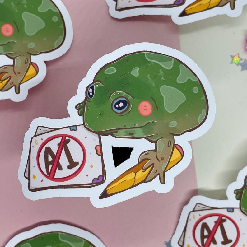 May include: A green frog with large eyes and a red circle with a diagonal line through the letters "AI" is holding a yellow pencil. The frog is sitting on a white piece of paper with a red circle with a diagonal line through the letters "AI".