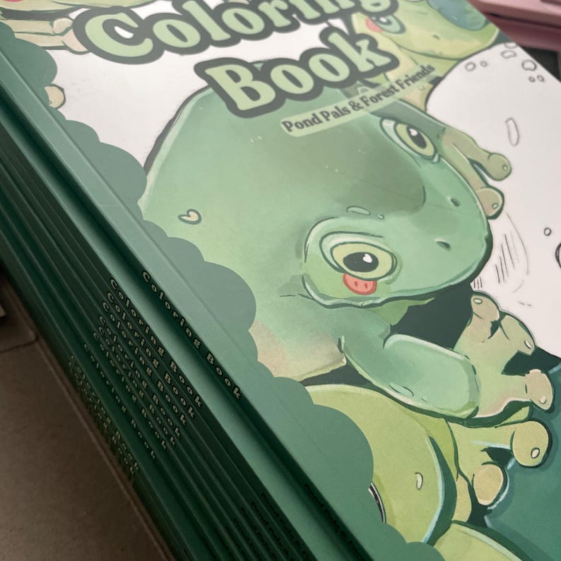 May include: A stack of coloring books with a green cover. The cover features a cartoon frog with the text "Coloring Book" and "Pond Pals & Forest Friends". The books have a green spine.