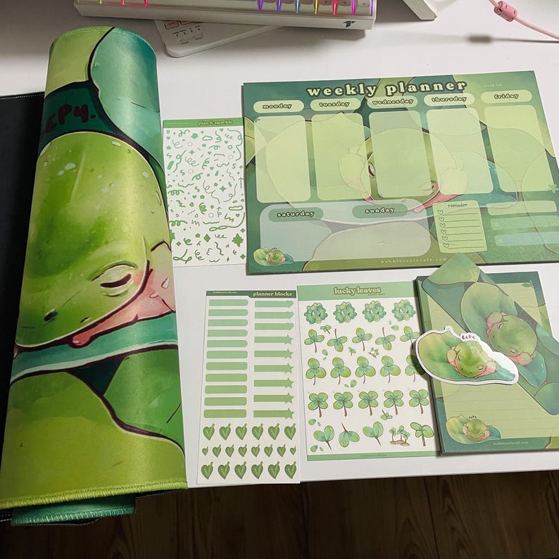 May include: A green frog themed weekly planner set with stickers. The set includes a planner, a sheet of planner blocks, a sheet of lucky leaves, and a sheet of hearts. The planner has a green frog design and the text "weekly planner" on the top. The stickers are all green and feature frogs, leaves, and hearts.