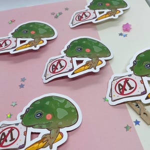 May include: Five green frog stickers with big eyes and a pencil. Each frog is holding a piece of paper with a red circle and the text "AI" with a line through it.