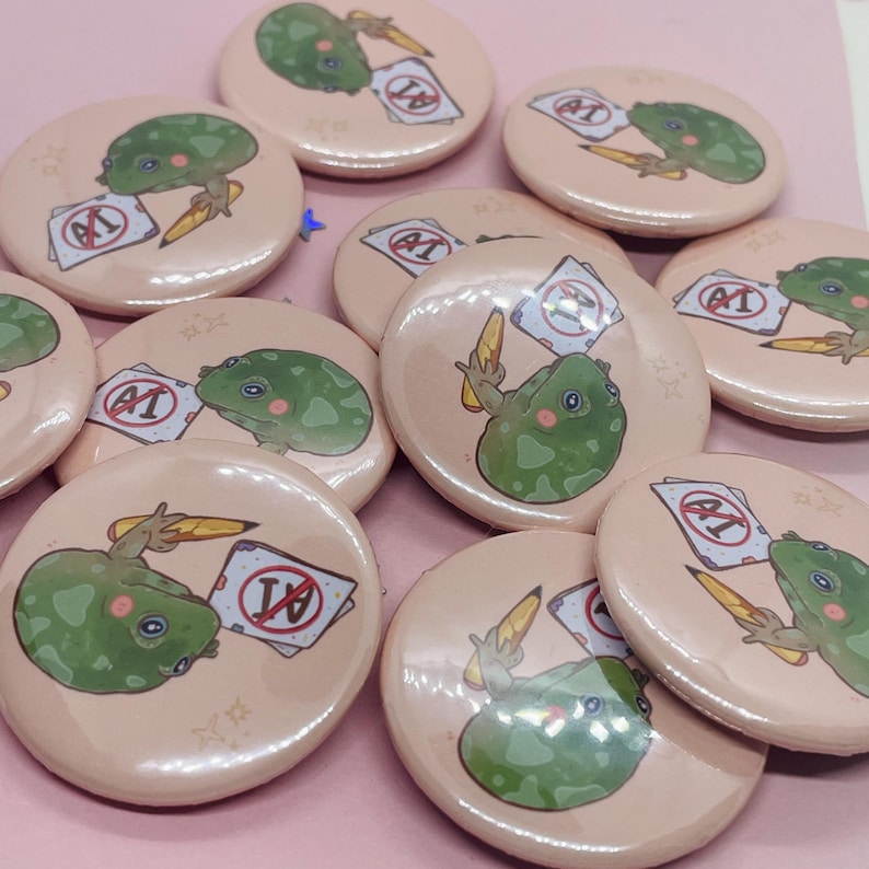 May include: A set of 10 round, pink button pins featuring a cartoon frog holding a pencil and a paper with a red circle and the letter 'F' inside. The frog is green with white eyes and a pink tongue. The background of the pins is a light pink with white stars.