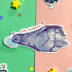 Op de afbeelding: Een sticker met een cartoon grijze duif die water drinkt uit een blauwe beker met de tekst "stay hydrated" in roze.