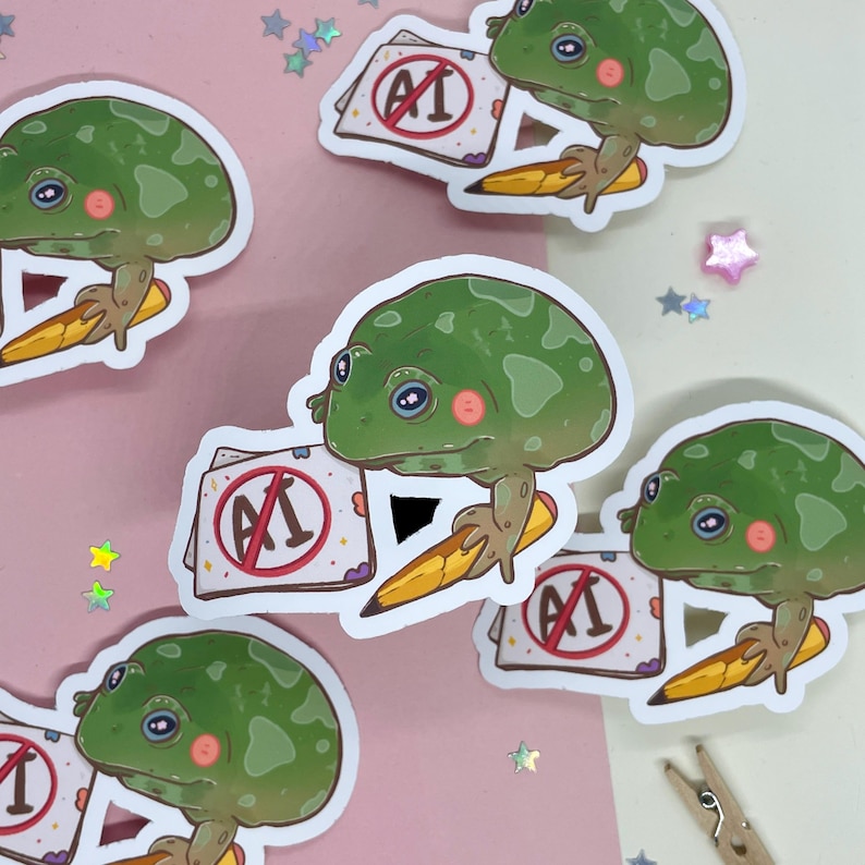 May include: Five stickers featuring a green frog holding a pencil and a paper with a red circle and the text "AI" with a diagonal line through it. The frog is holding a pencil and the paper is on a pink background.