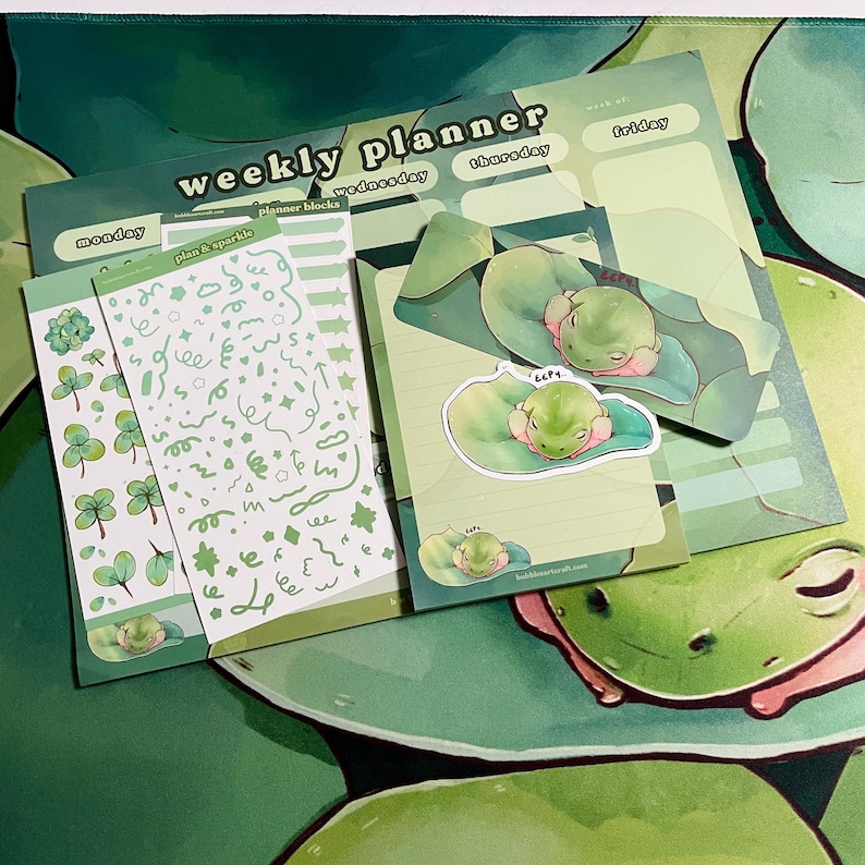 May include: A weekly planner with a green frog theme. The planner includes a cover sheet with the words "weekly planner" and sections for each day of the week. There are also several sticker sheets with green frogs, clover leaves, and other designs.