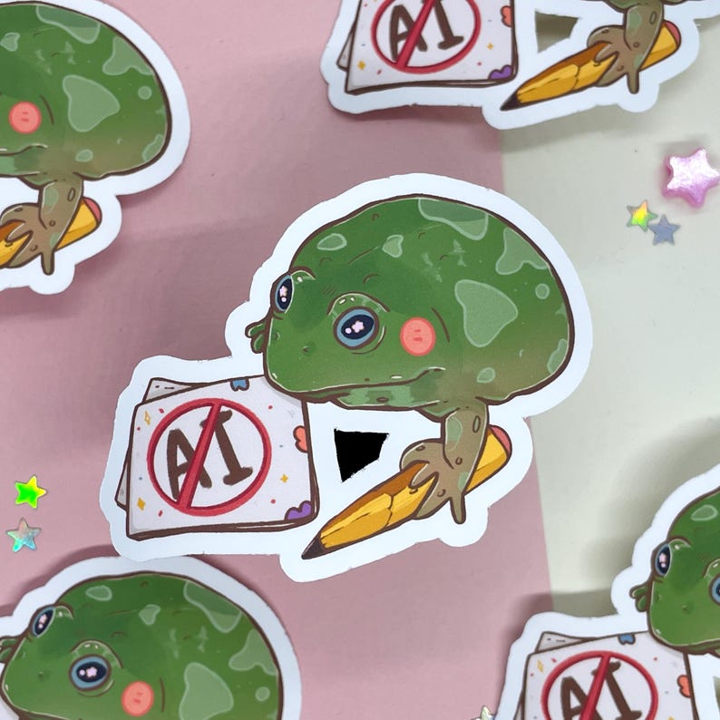 May include: A green frog with a red circle and a diagonal line through it, with the letter "A" inside the circle. The frog is holding a yellow pencil and is sitting on a white sticker with a pink and white background.