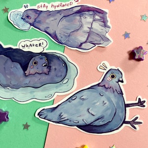Op de afbeelding: Drie stickers met cartoon-duiven. E&eacute;n sticker toont een duif die water drinkt uit een glas, met de tekst "stay hydrated". Een andere sticker toont een duif die badt in een blauwe badkuip, met de tekst "whatever!" De derde sticker toont een duif met zijn vleugels uitgespreid, die er verbaasd uitziet.