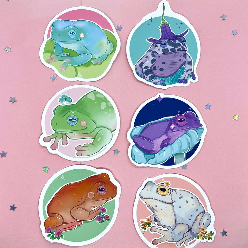 May include: Set of six frog stickers featuring different frog species in various poses. The stickers are on a pink background and feature a variety of colors, including green, blue, purple, and brown.