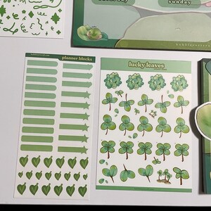 May include: Two sticker sheets with green shamrock and leaf designs. The first sheet has the text "planner blocks" and features green rectangles, stars, and hearts. The second sheet has the text "lucky leaves" and features various green shamrock designs.