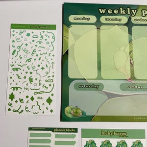 May include: A set of green and white planner stickers with a weekly planner page in the background. The stickers include a sheet of green doodles, a sheet of planner blocks, and a sheet of lucky leaves.