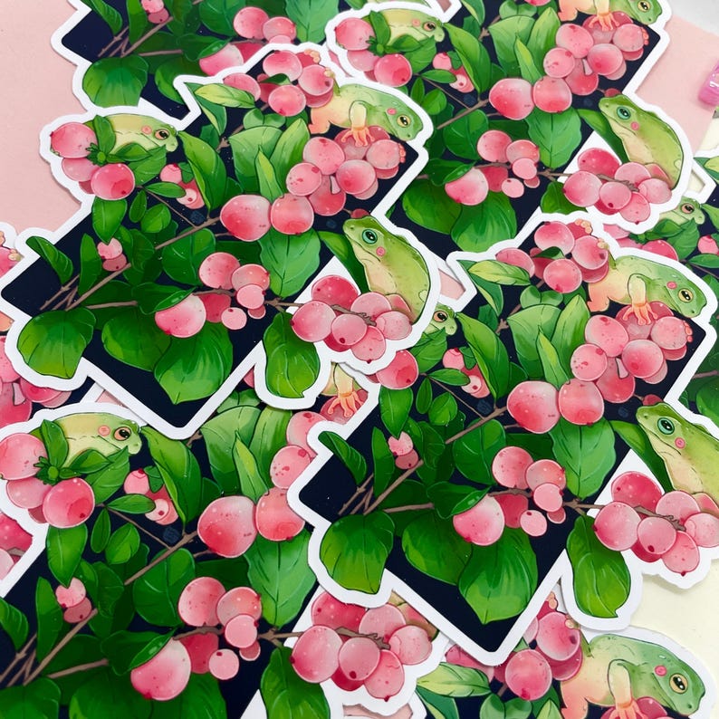 Puede incluir: Colecci&oacute;n de pegatinas con una rana verde posada entre bayas rosas y hojas verdes. Las pegatinas tienen un borde blanco y est&aacute;n colocadas sobre un fondo oscuro con un dise&ntilde;o geom&eacute;trico blanco.