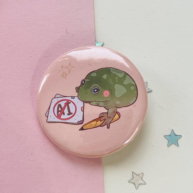 May include: A pink button with a green frog holding a pencil and a piece of paper with a red circle and a diagonal line through the letters "AI".