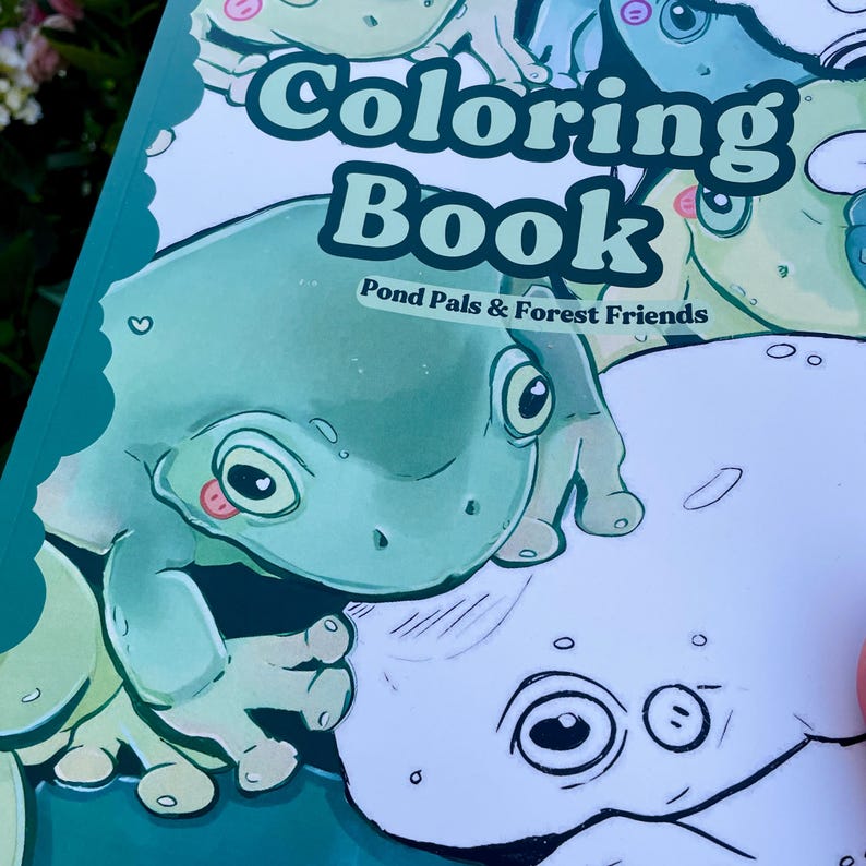 May include: A coloring book titled "Coloring Book" with the subtitle "Pond Pals & Forest Friends." The cover features a cartoon frog in shades of green and white. The frog has large eyes and a pink tongue. The book is open, revealing a partially colored page.