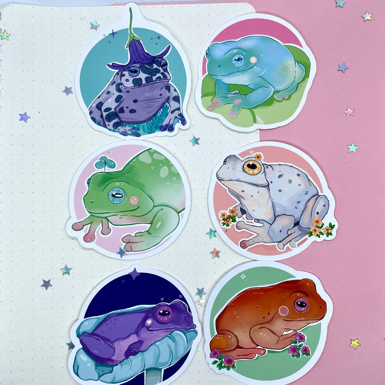 May include: Set of six frog stickers with different colored frogs and floral designs. The frogs are in various poses, including sitting, jumping, and swimming. The stickers are perfect for adding a touch of whimsy to your planner, laptop, or water bottle.