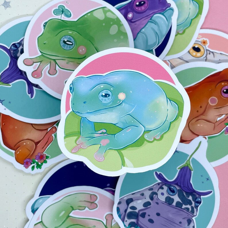 May include: A set of nine frog stickers with various colors and designs. The stickers feature frogs in different poses, including sitting, jumping, and swimming. Some stickers have a floral design, while others have a more abstract design.