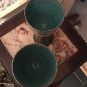 Könnte beinhalten: Zwei teal-farbene Keramikbecher mit Metallrand. Die Becher stehen auf einem dunklen Holztisch mit Marmorplatte. Die Innenseite der Becher hat eine einzigartige Textur.