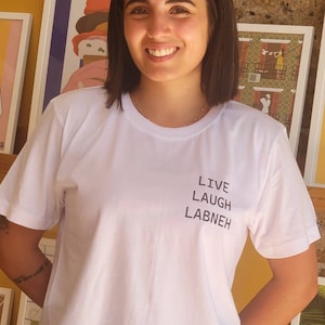 May include: A woman wearing a white t-shirt with the text "LIVE LAUGH LABNEH" printed on it.
