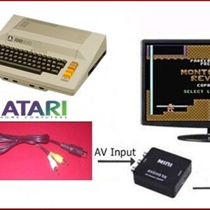 May include: A beige Atari 800 computer with a black keyboard and a yellow and orange joystick. The computer is connected to a black monitor displaying the video game "Montezuma's Revenge" by Parker Brothers. The game screen shows the title, copyright date, and level selection options. A black AV cable with yellow and red RCA connectors is shown in the image.