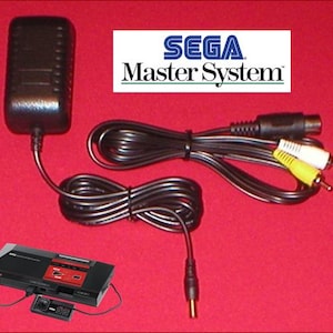 May include: A black Sega Master System console with a controller, power adapter, and AV cables. The Sega Master System logo is displayed on a white rectangle. The console is black and red.